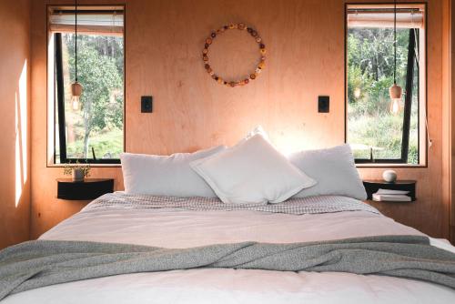 a bedroom with a bed with white pillows and a mirror at Koa Cabin Hahei in Hahei