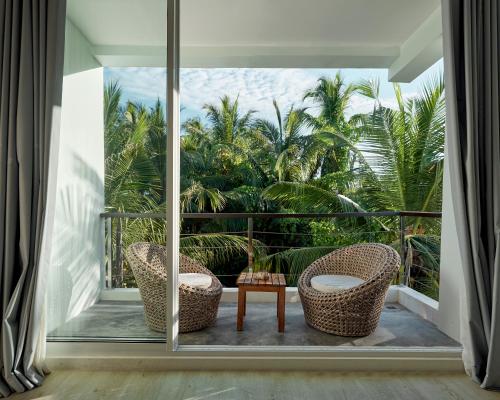 a balcony with two chairs and a table and palm trees at Bliss Dhigurah in Dhigurah