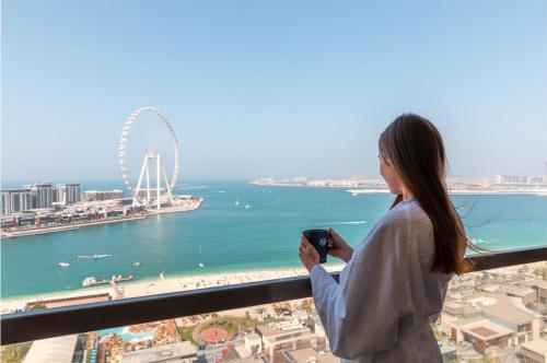 a woman looking at her cell phone in front of the ocean at Amwaj Rotana, Jumeirah Beach - Dubai in Dubai