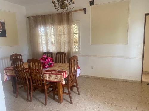 una sala da pranzo con tavolo, sedie e finestra di MANOIR DES PRINCESSES BAFOUSSAM a Bafoussam