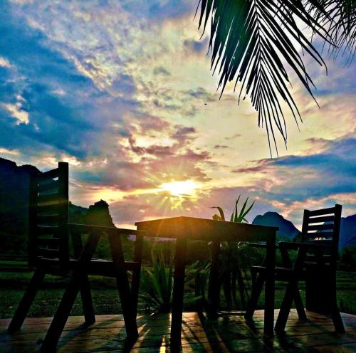 une table et des chaises avec le coucher du soleil en arrière-plan dans l'établissement Vang Vieng Savanh Sunset View Resort, à Vang Vieng