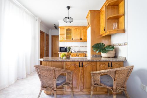 a kitchen with wooden cabinets and wicker chairs at Home2Book Stylish Apartment Caletillas in Candelaria