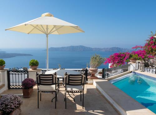 a table with an umbrella and chairs next to a swimming pool at Lithies Traditional Homes in Firostefani