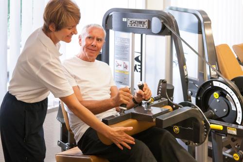 a woman helping an older man in a gym at Park-Hotel am Rhein - Gesundheitshotel und Residenzen in Rheinfelden