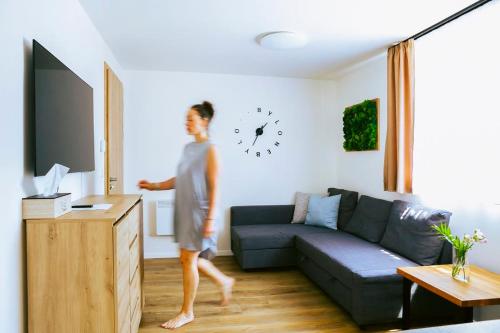 a woman walking through a living room with a clock on the wall at Bylo Nebylo apartmány in Vítkovice