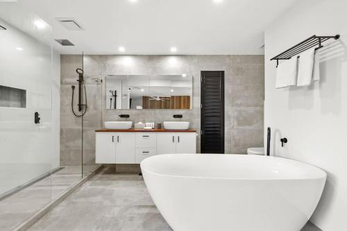 uma casa de banho branca com uma banheira e um chuveiro em Ultra Modern & Relaxing Inner City 4bed House - with a Private Pool - 10mins walk to Beach em Gold Coast