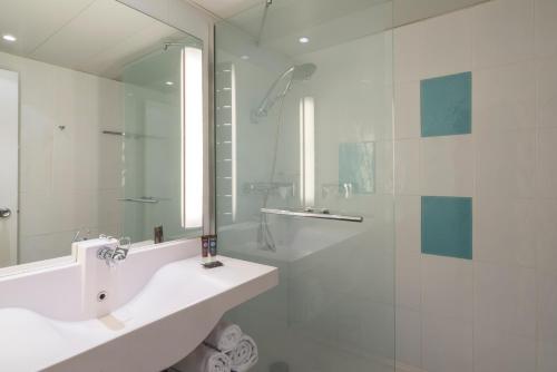 a white bathroom with a sink and a shower at Novotel Dijon Sud in Marsannay-la-Côte