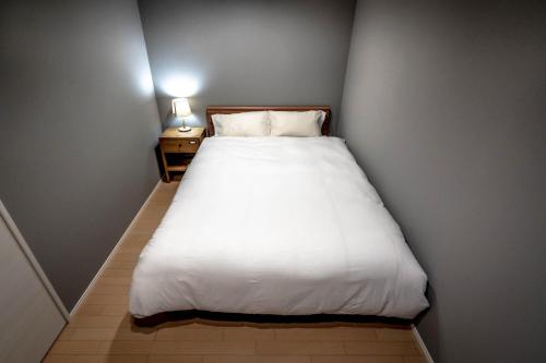 a small bedroom with a white bed and a night stand at Rakuten STAY HOUSE x WILL STYLE Hachimanbori in Omihachiman