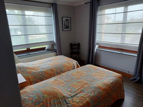 two beds in a room with two windows at Le Reposoir Maison spacieuse avec feu au bois in Bertogne
