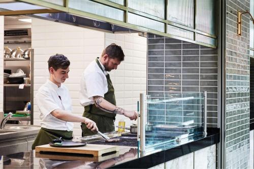 two chefs standing in a kitchen preparing food at Hyatt House Manchester - Aparthotel in Manchester