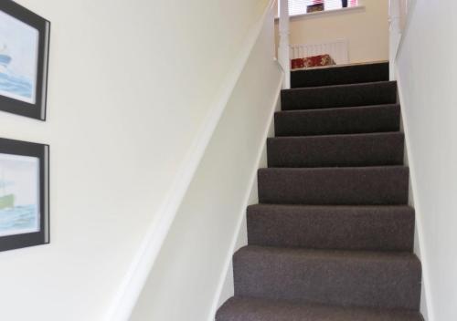 a staircase in a house with grey carpet and pictures at The Little Hopton in Saxmundham