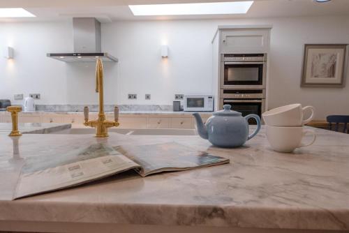 a kitchen counter with a newspaper and a teapot on a table at The Pink House in Southwold - Air Manage Suffolk in Southwold