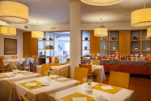 a restaurant with white tables and yellow chairs at Hotel Romanda in Levico Terme