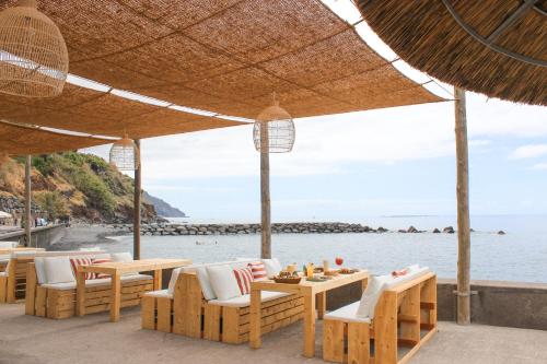 a beach with chairs and tables and a view of the water at Saccharum - Resort and Spa - Savoy Signature in Calheta