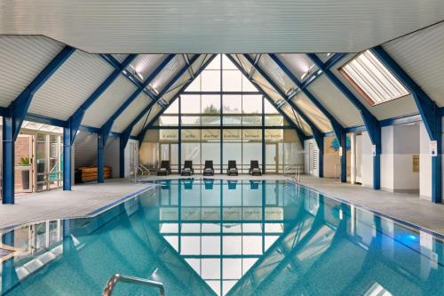 une grande piscine avec des baies vitrées et une piscine intérieure dans l'établissement Ufford Park Resort, à Woodbridge
