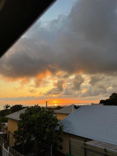 a cloudy sky with the sun setting behind houses at La Grenad'Île in Saint-Pierre