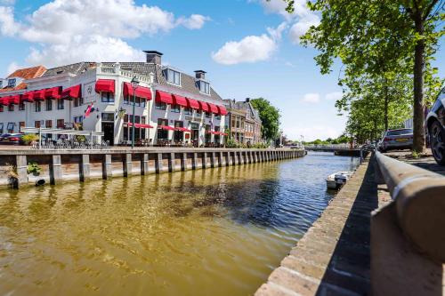 een rivier met een gebouw met rode luifels bij Hotel Restaurant 't Heerenlogement in Harlingen