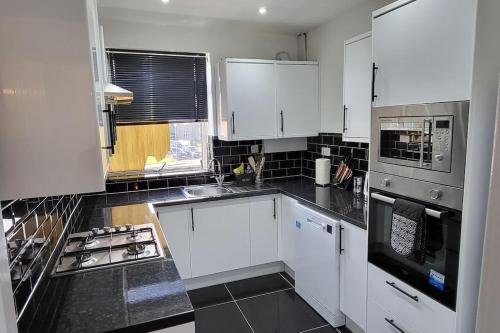 a kitchen with white cabinets and black counter tops at Newly refurbished 3 bedroom flat in Bedworth