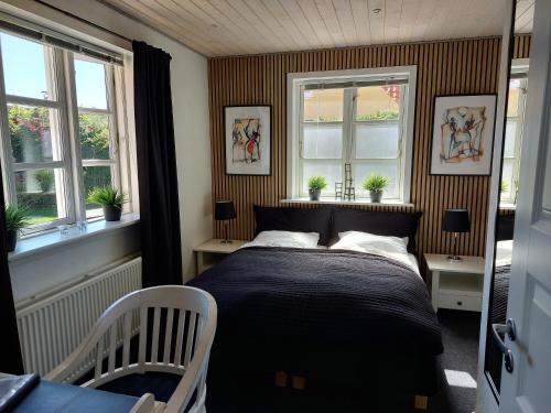 a bedroom with a bed and two windows at Toftegården Guesthouse - Rooms in Skagen