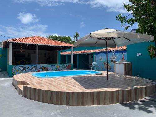 a swimming pool with an umbrella next to a house at Pousada Verdes Mares Porto De Galinhas in Porto De Galinhas