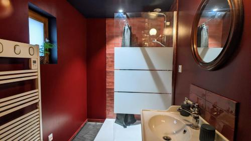 La salle de bains est pourvue de murs rouges, d'un lavabo et d'un miroir. dans l'établissement Le Cottage et la Tiny des Cartes - 2 maisons, à LʼÎle Bouchard
