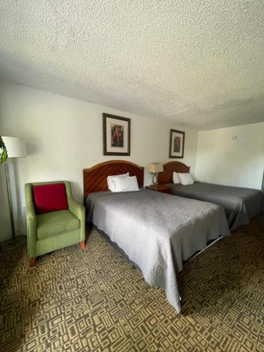 a hotel room with two beds and a green chair at Ambassador Inn in Kissimmee
