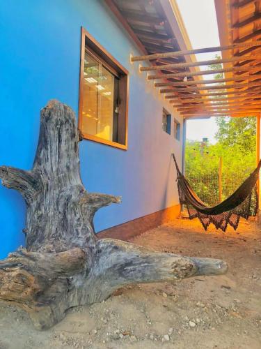 a tree stump with a hammock in front of a house at Vila Verde Chalés-Serro in Sêrro