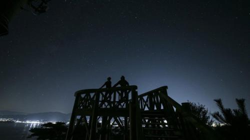 two people sitting on top of a wooden structure at night at Kyukamura Kesennuma-Ohshima in Kesennuma