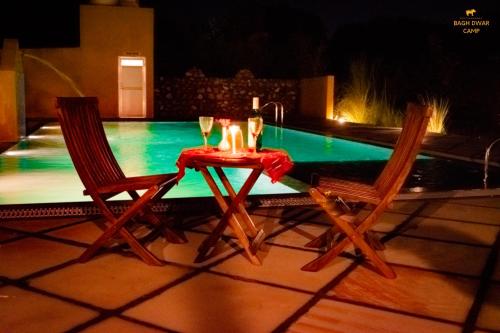 a table with two chairs and wine glasses next to a pool at Ranthambhore Bagh Dwar Camp in Khilchipur