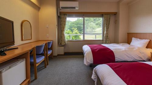 a hotel room with two beds and a desk and a television at Kyukamura Taishakukyo in Shōbara