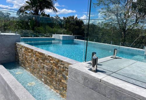 a swimming pool with a stone wall next to a building at Sinclairs Country Retreat in Conjola