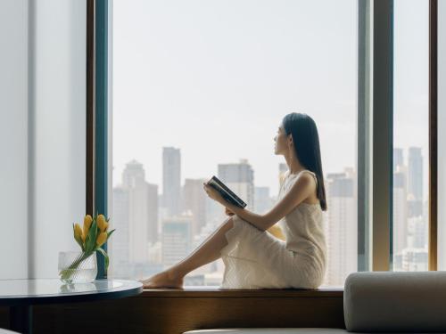 a woman sitting on a window sill reading a book at Andaz Xiamen, By Hyatt in Xiamen
