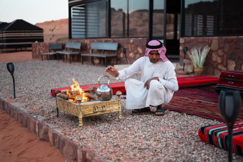 a man sitting on the ground next to a fire at Milky Way Bedouin Camp in Wadi Rum