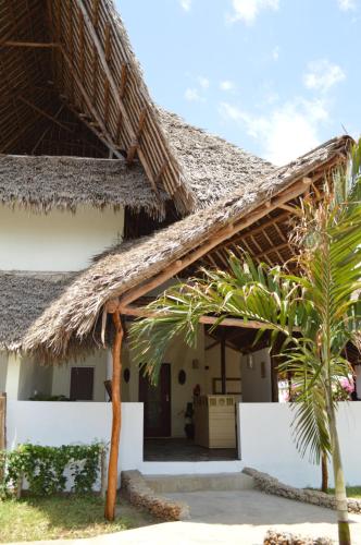 a house with a thatched roof and a palm tree at Pole Pole Beach House in Watamu