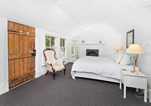 ein weißes Schlafzimmer mit einem Bett und einem Stuhl in der Unterkunft Boat Harbour Store Cottage in Gerringong