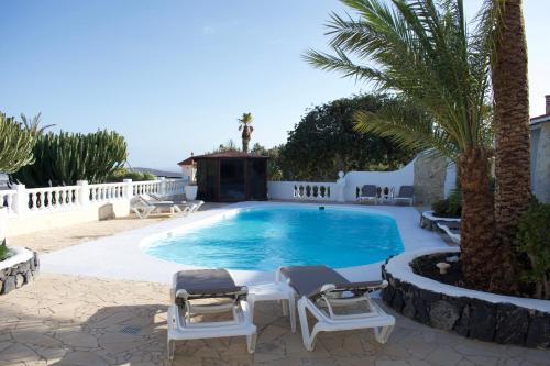 a swimming pool with two chairs and a palm tree at Wohnung Aulaga in Agüimes