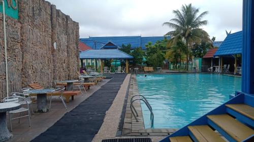 a swimming pool with tables and chairs next to a building at Capital O 91806 Hotel Batu Suli in Palangkaraya