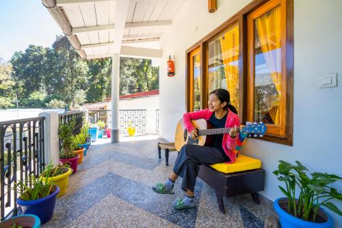 a woman sitting on a chair playing a guitar on a porch at goSTOPS Nainital in Nainital