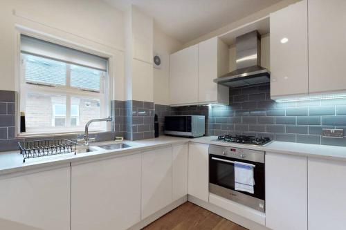 a kitchen with white cabinets and a sink and a stove at Lovely 2-bedroom flat with parking near Highgate in London