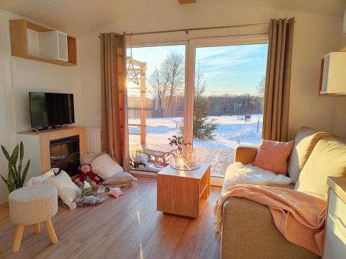a living room with a fireplace and a large window at Giżycko - Żywki, Masuria Resort Village, całoroczne domki z widokiem na jezioro in Żywki