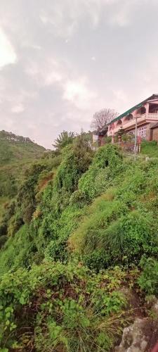 a grassy hill with a house on top of it at Ritu Raj Home Stay & Cafe in Malther