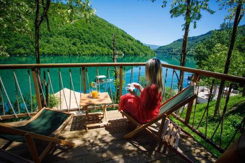 a woman sitting in a chair on a deck overlooking a lake at Glamping Bagrem in Jablanica