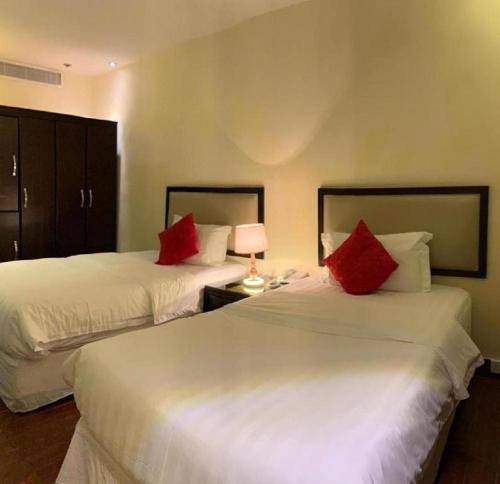 two beds in a hotel room with red pillows at فندق البروج الفندقية in Jazan