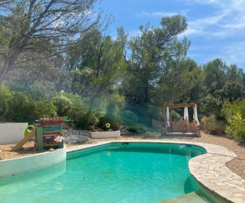 una piscina en un patio con parque infantil en Avignon : Le Mas Cott, le paradis dans la nature, en Aramon
