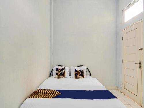 Dormitorio blanco con cama con almohadas azules y amarillas en SPOT ON 91834 Sg 99 Homestay Syariah en Parit