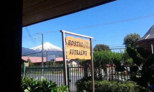 a sign in front of a building with a mountain in the background at Hostal Kutralwe in Pucón
