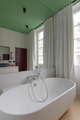 La salle de bains est pourvue d'une grande baignoire blanche et d'un miroir. dans l'établissement MiHotel Blandan, à Lyon