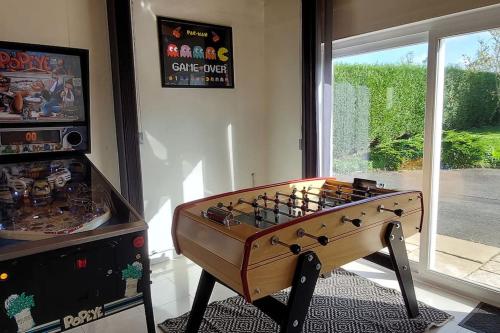 a foosball table in a room next to a window at Grande maison , jardin,flipper,babyfoot, ping pong, 1 km mer, proche golf, Port en Bessin, Bayeux et plages du débarquement, adaptée enfants in Commes