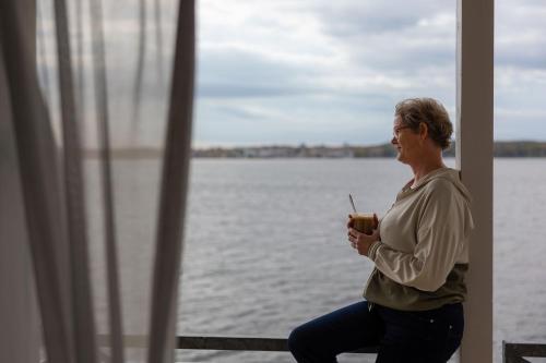 a woman sitting next to the water holding a drink at Hørby Færgekro in Holbæk