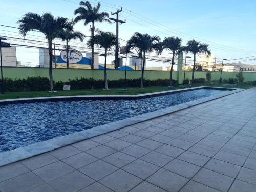 a swimming pool with palm trees in front of a building at Ponta Negra RN02 in Natal